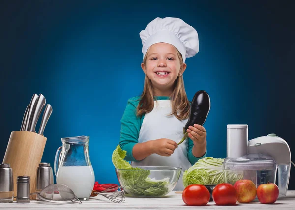 Girl Chef bereidt een heerlijk gerecht op een blauwe achtergrond. — Stockfoto