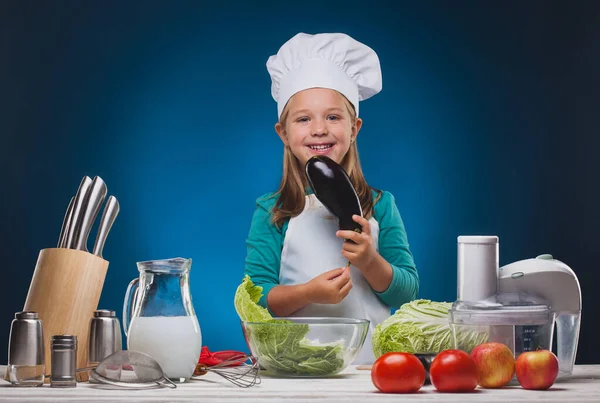 Chica Chef prepara un delicioso plato sobre un fondo azul . —  Fotos de Stock