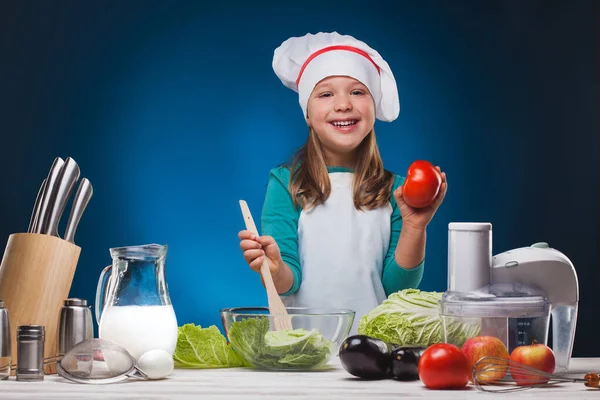 Girl Chef bereidt een heerlijk gerecht op een blauwe achtergrond. — Stockfoto