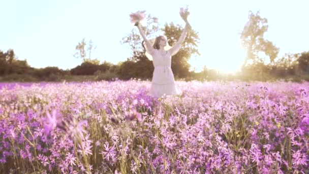 Молодая женщина с букетом полевых цветов стоит на солнечном цветущем лугу — стоковое видео