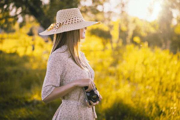 girl photographer in a sunny meadow with a retro camera takes a photo of the landscape