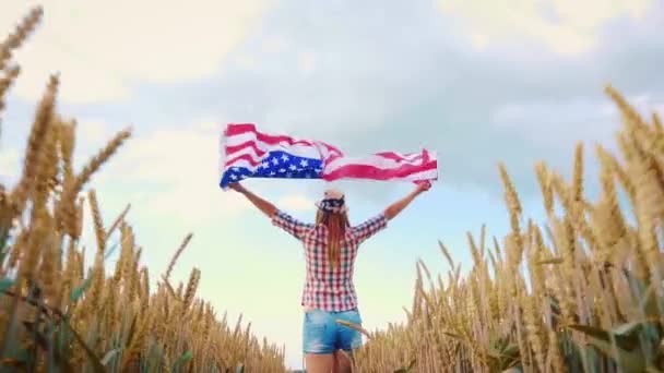 菜の花畑でアメリカ国旗を掲揚している美しい少女 青空に対する夏の風景 独立記念日7月4日 動画クリップ