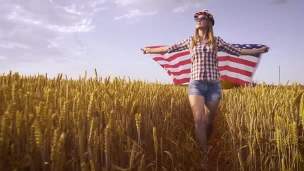 菜の花畑でアメリカ国旗を掲揚している美しい少女 青空に対する夏の風景 独立記念日7月4日 ロイヤリティフリーストック映像