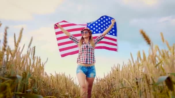 菜の花畑でアメリカ国旗を掲揚している美しい少女 青空に対する夏の風景 独立記念日7月4日 ストック映像