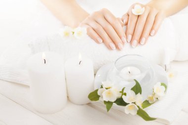 Beyaz ahşap masada yasemin, mum ve havluyla güzel bir Fransız manikürü..