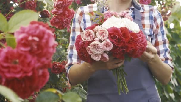 Kvinna trädgårdsmästare med en bukett rosor i en blommande trädgård — Stockvideo