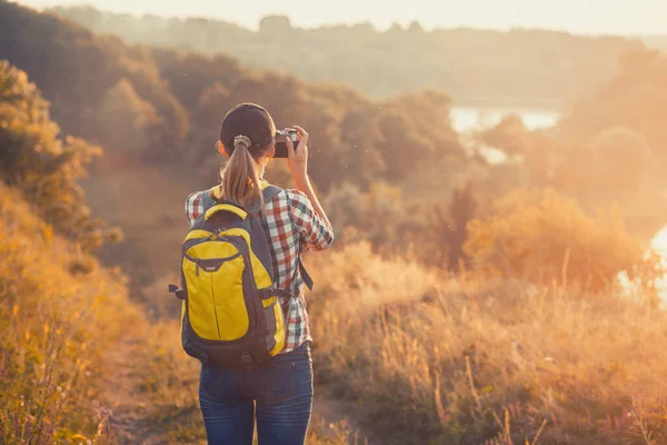 带着背包和照相机的女游客穿过风景如画的草地 给风景如画的风景拍照 户外活动 — 图库照片