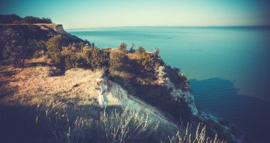 Uçurumun kenarındaki şapkalı güzel genç bir kadın. Bir buket çiçekli retro şapkalı..