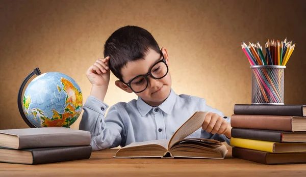 Милый маленький мальчик школьник делает домашнее задание за столом с книгами — стоковое фото