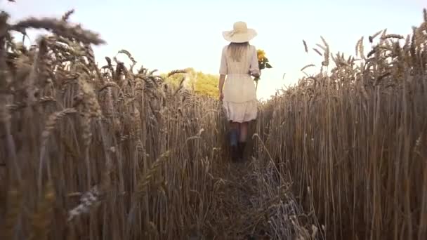 Frau mit Sonnenblumen im Retro-Kleid und Hut in einem Sommerweizenfeld — Stockvideo