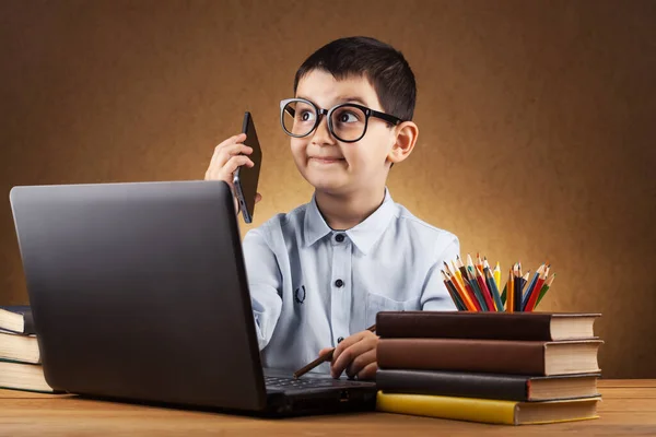 Lindo pequeño hombre de negocios haciendo con el ordenador portátil en la mesa con libros —  Fotos de Stock