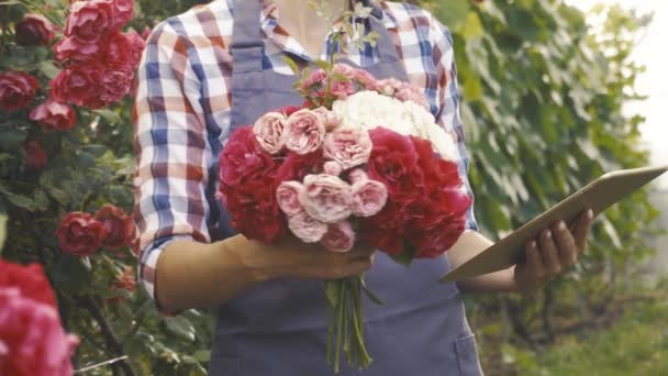 Vrouw tuinier met een boeket van rozen in een bloeiende tuin — Stockvideo
