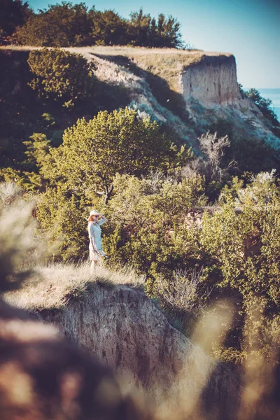 Woman in a hat on a high sea cliff with a bouquet of flowers in a retro hat. — Stock Photo, Image