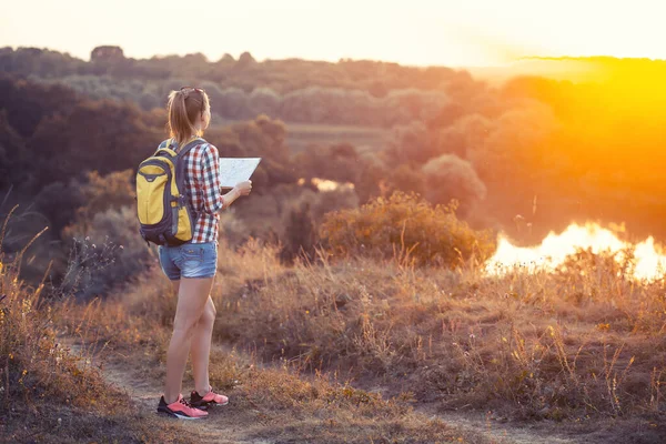 Kvinna turist med en karta och en ryggsäck på en vandring navigerar terrängen. Fritid — Stockfoto