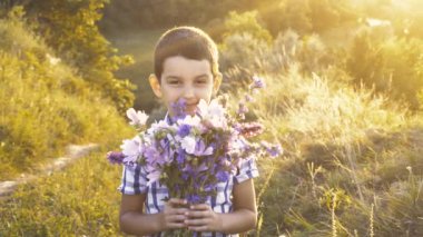 Bir buket kır çiçeğiyle yaz otlağında tatlı bir çocuk.