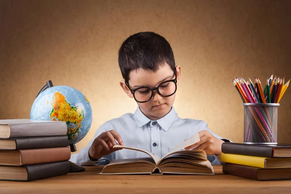 Cute little boy schoolboy doing homework at a table with books — Stock Photo, Image