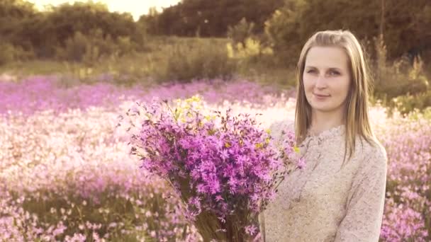 Jovem com um buquê de flores silvestres em pé em um prado ensolarado — Vídeo de Stock