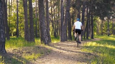 Bisikletli adam orman yolunda gidiyor.