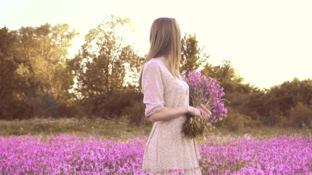 Jovem com um buquê de flores silvestres em pé em um prado ensolarado — Vídeo de Stock