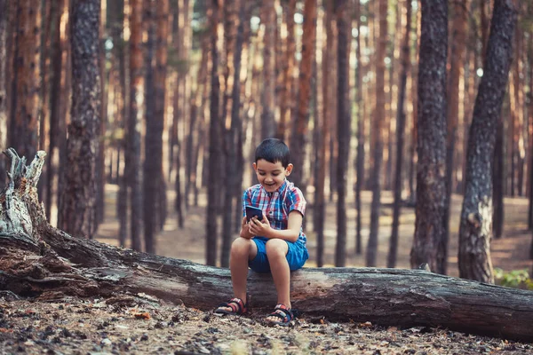 Menino em uma pitoresca floresta de pinheiros brincando com um smartphone — Fotografia de Stock