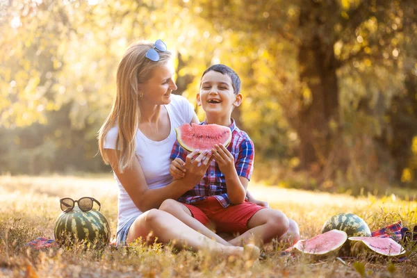 Niño feliz con mamá comiendo sandía madura en el parque de verano —  Fotos de Stock
