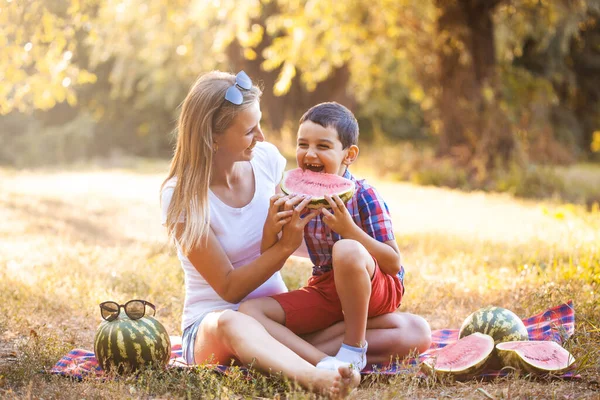 Niño feliz con mamá comiendo sandía madura en el parque de verano —  Fotos de Stock