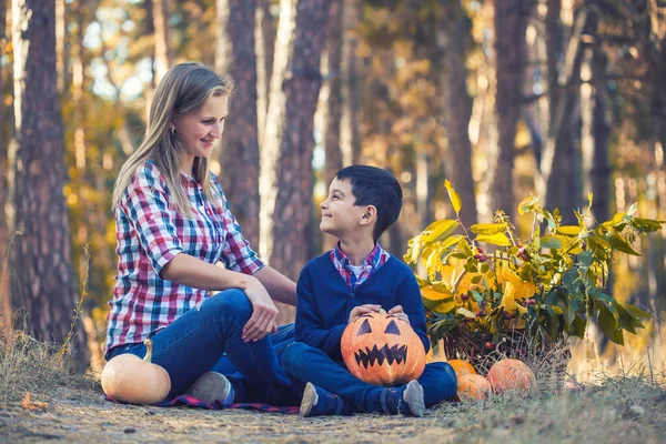 Miúdo bonito com mãe esculpida abóbora para halloween em uma floresta de pinheiros — Fotografia de Stock