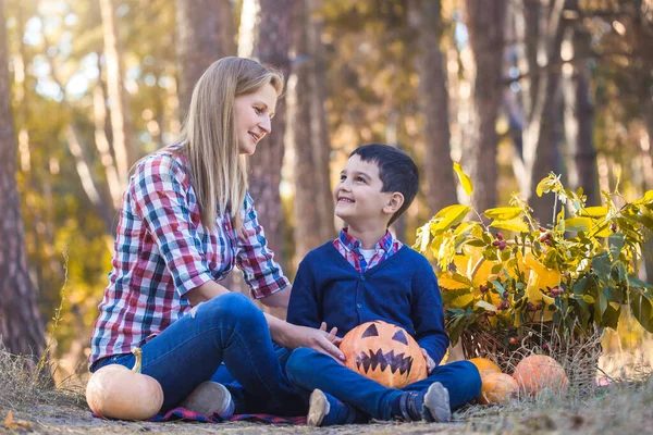 Lindo niño con mamá tallada calabaza para Halloween en un bosque de pinos — Foto de Stock