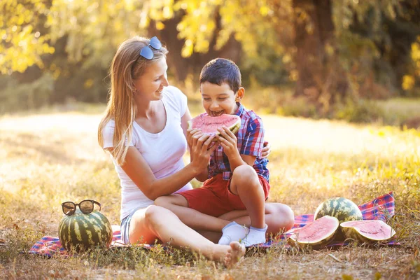 Счастливый мальчик с мамой едят спелый арбуз в летнем парке — стоковое фото
