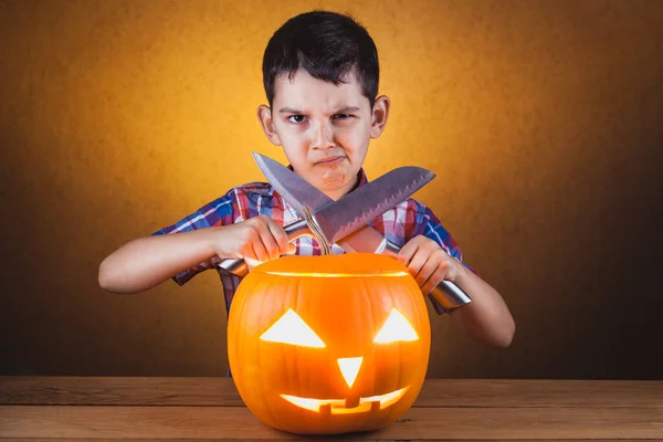 angry little boy carves a pumpkin with knives.