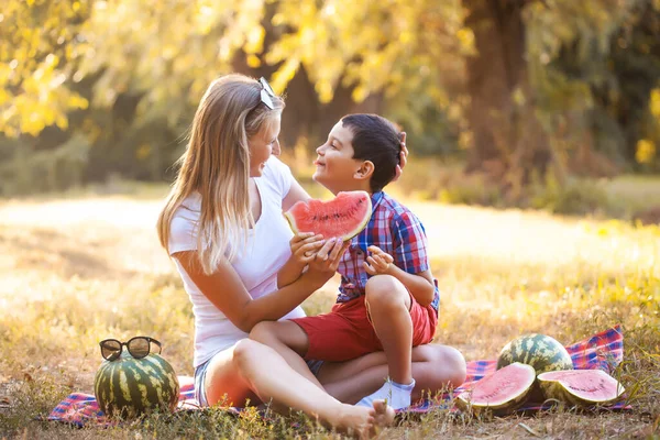 Niño feliz con mamá comiendo sandía madura en el parque de verano —  Fotos de Stock