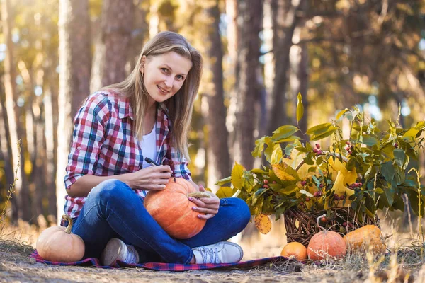 Pretty woman paints a pumpkin in a pine forest. — Stock Photo, Image