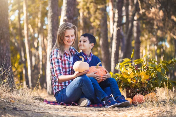 Miúdo bonito com mãe esculpida abóbora para halloween em uma floresta de pinheiros — Fotografia de Stock