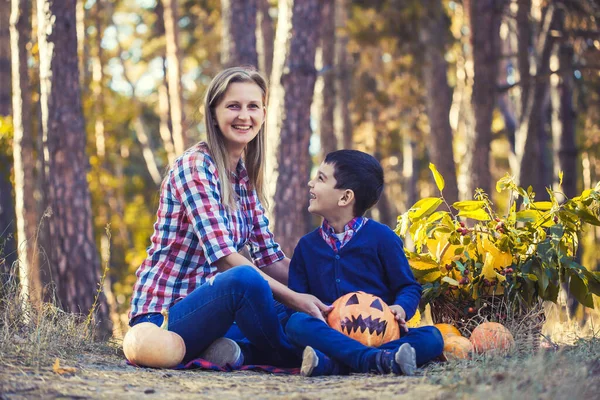 Niedliches Kind mit Mama geschnitzt Kürbis für Halloween in einem Kiefernwald — Stockfoto