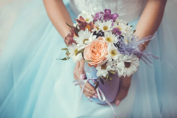 Vrouwelijke handen met een doos bloemen op de achtergrond van een witte trouwjurk. — Stockfoto