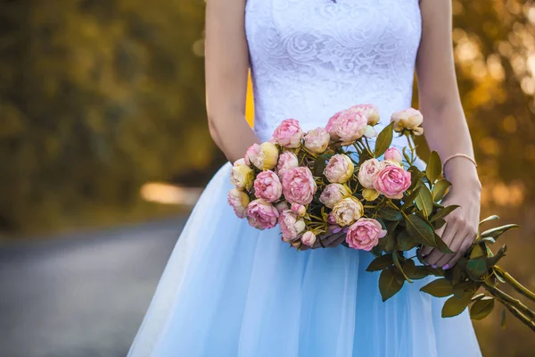 Mani femminili con fiori sullo sfondo di un abito da sposa bianco. — Foto Stock