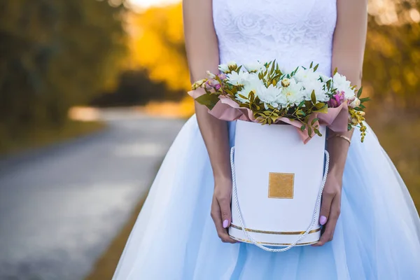 Mani di spose con fiori in una scatola regalo su uno sfondo di fogliame di autunno. — Foto Stock