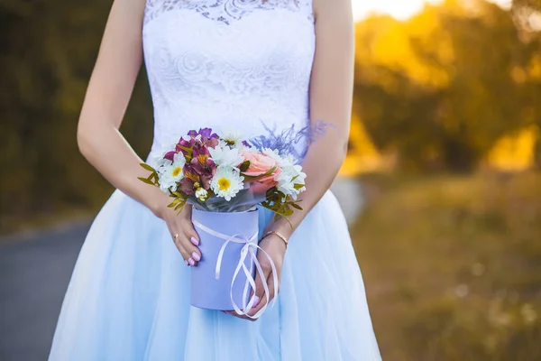 Mãos femininas com uma caixa de flores no fundo de um vestido de noiva branco. — Fotografia de Stock