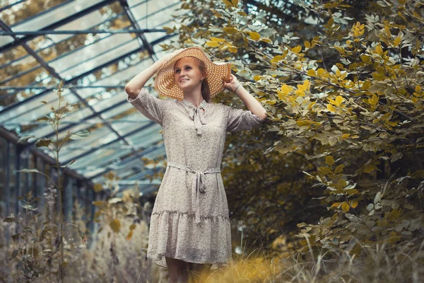 Woman with a bouquet of dried flowers in a retro dress and a hat in a old greenhouse — Stock Photo, Image