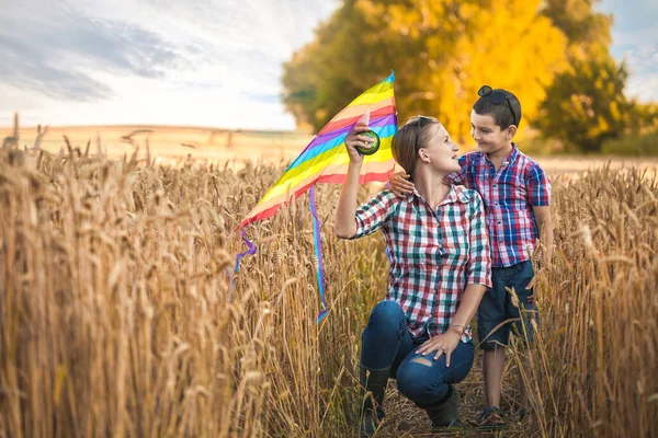 Мама и сын запускают воздушного змея на летнем пшеничном поле — стоковое фото