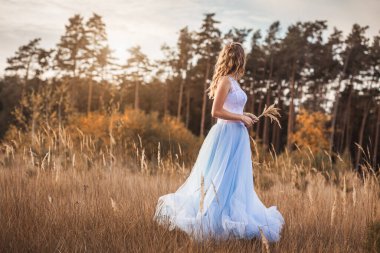 Bir buket çiçekli mutlu gelin sonbahar çayırında yürüyor.