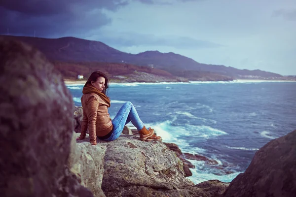 Mujer joven sentada en una roca cerca del mar —  Fotos de Stock