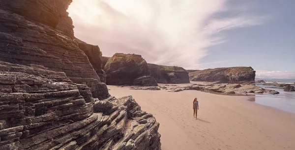 Mujer joven en bikini dando un paseo por una playa llena de acantilados rocosos en Ribadeo, Galicia —  Fotos de Stock