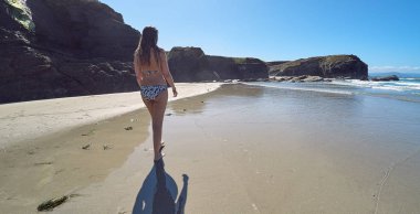 Galiçya, İspanya'da kayalıklarla bir plajda yürüyen genç kadın