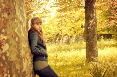 Sonbaharda ağaca yaslanan genç bir kadın.