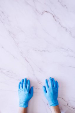 Tıbbi eldivenli bir çift elin üst görüntüsü beyaz mermer arka planda bolca fotokopi alanı var.