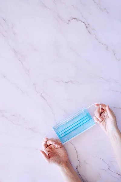 Hands holding a surgery mask against a marble background with plenty of copy space