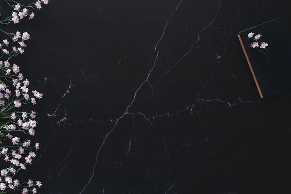 Çiçek aranjmanı, ahşap bir parça ve bolca fotokopi alanı olan siyah mermere karşı bir kitap.