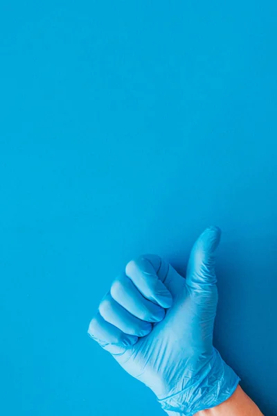 Tıbbi eldivenli bir el, mavi arka planda bir sürü fotokopi alanı olan bir jest yapıyor.