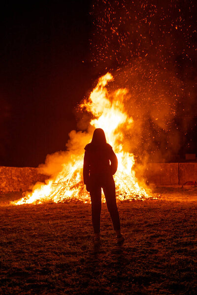Silhouette of a woman contemplating a giant bonfire, typical spanish celebration of the summer solstice, calling it the night of San Juan, or St. John